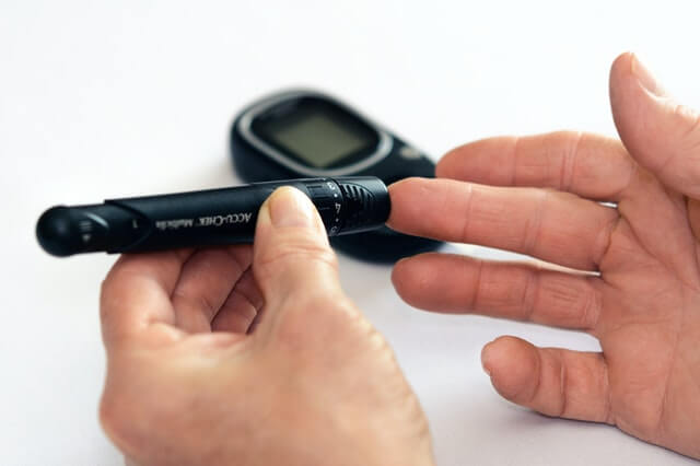 Image of a black Accu-Chex blood glucose monitor held in a left hand, pricking the right with the actual monitor in the background. Photo by PhotoMIX Company from Pexels